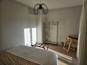 A bedroom with a bed, a hanging light fixture, a wooden chair, and a shelf unit.