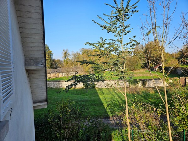 A view of a grassy area with a stone wall and trees, a building with a sloped roof, and a clear blue sky.