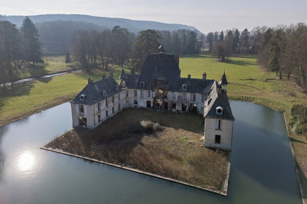 A large, historic building with a central courtyard, surrounded by water and trees.