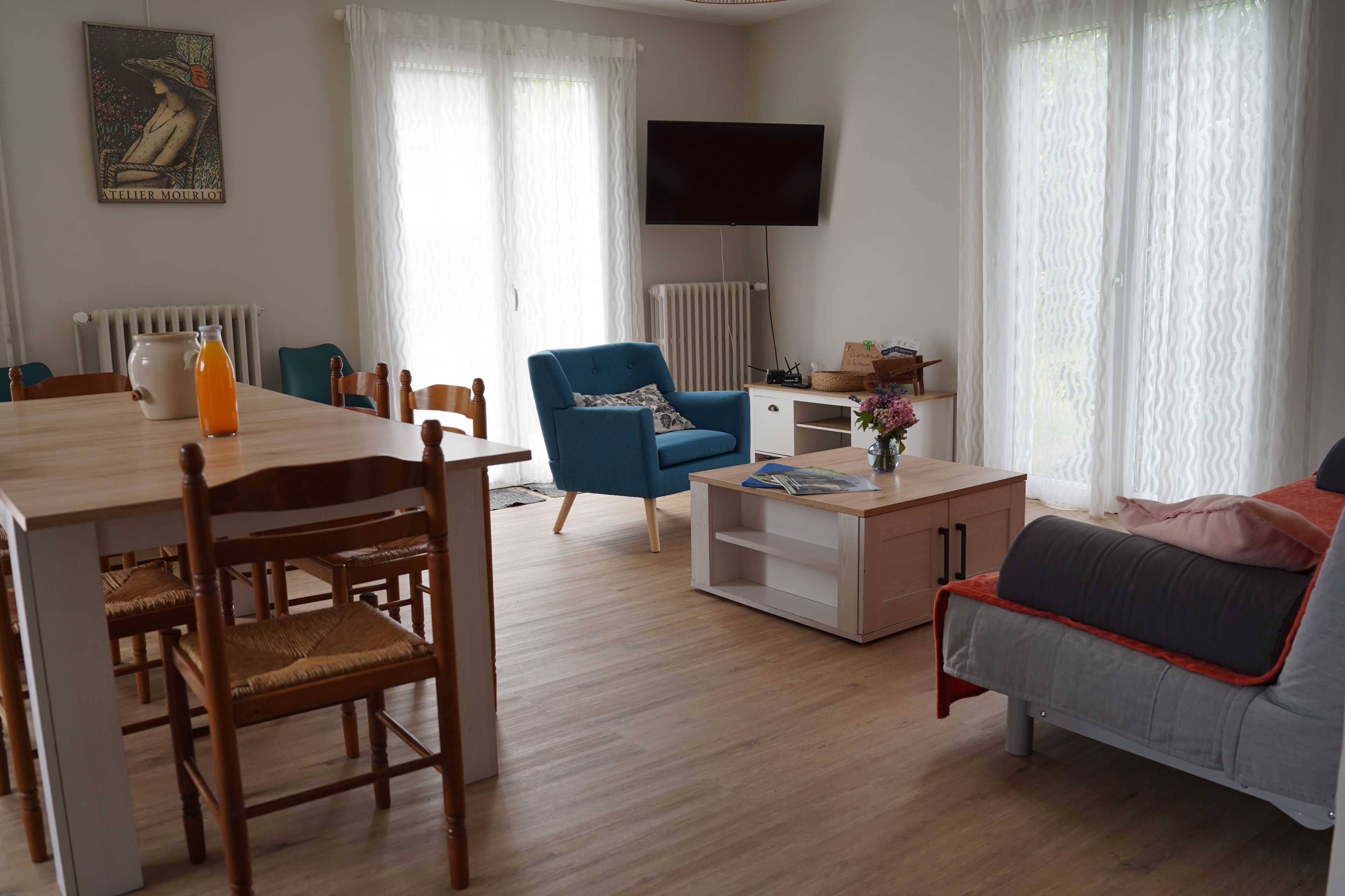 A modern living room with a dining area, a blue armchair, a sofa, and a television mounted on the wall.