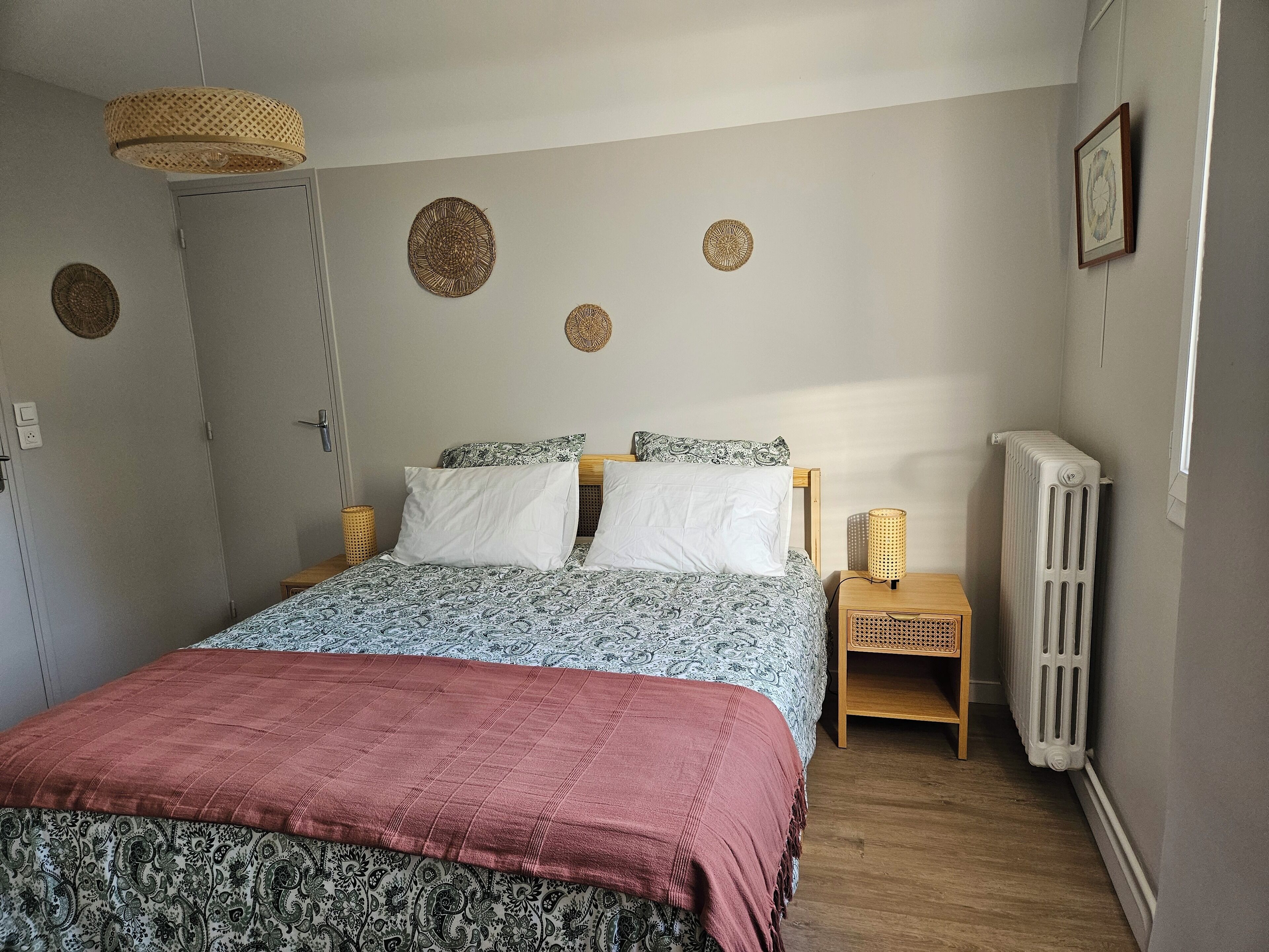 Een slaapkamer met een bed, nachtkastjes, een radiator en decoratieve wandversieringen.