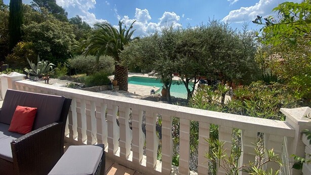 Ein Balkon mit Blick auf ein Schwimmbecken, umgeben von Bäumen und Pflanzen.