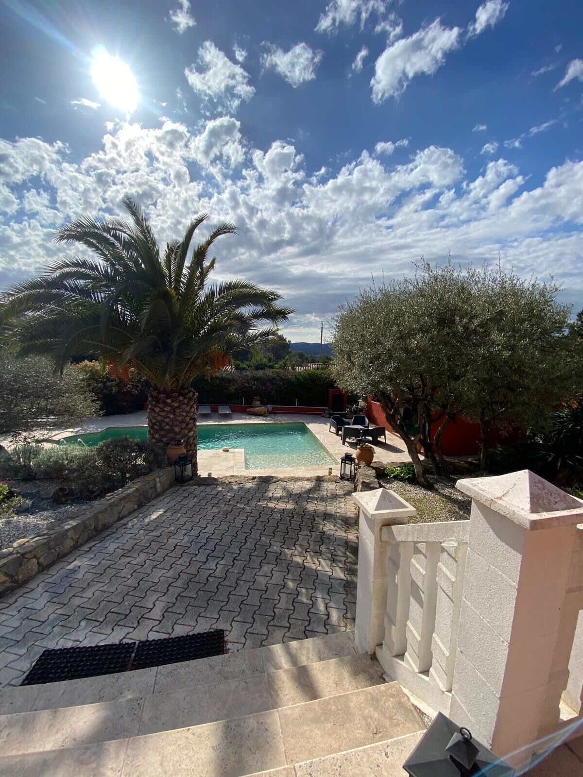 A pool area with a clear view of the sky, a palm tree, and a stone pathway leading to the pool.