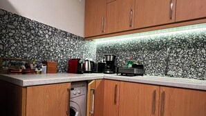 Eine Küche mit Holzausstattung, einer Waschmaschine, einer Kaffeemaschine und einer gefliesten Spritzschutzwand.