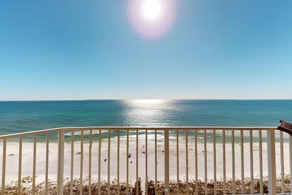 A beach view from a balcony with a railing, ocean, and clear sky.