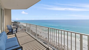 Un balcon avec vue sur l’océan et la plage, une chaise bleue et un canapé.