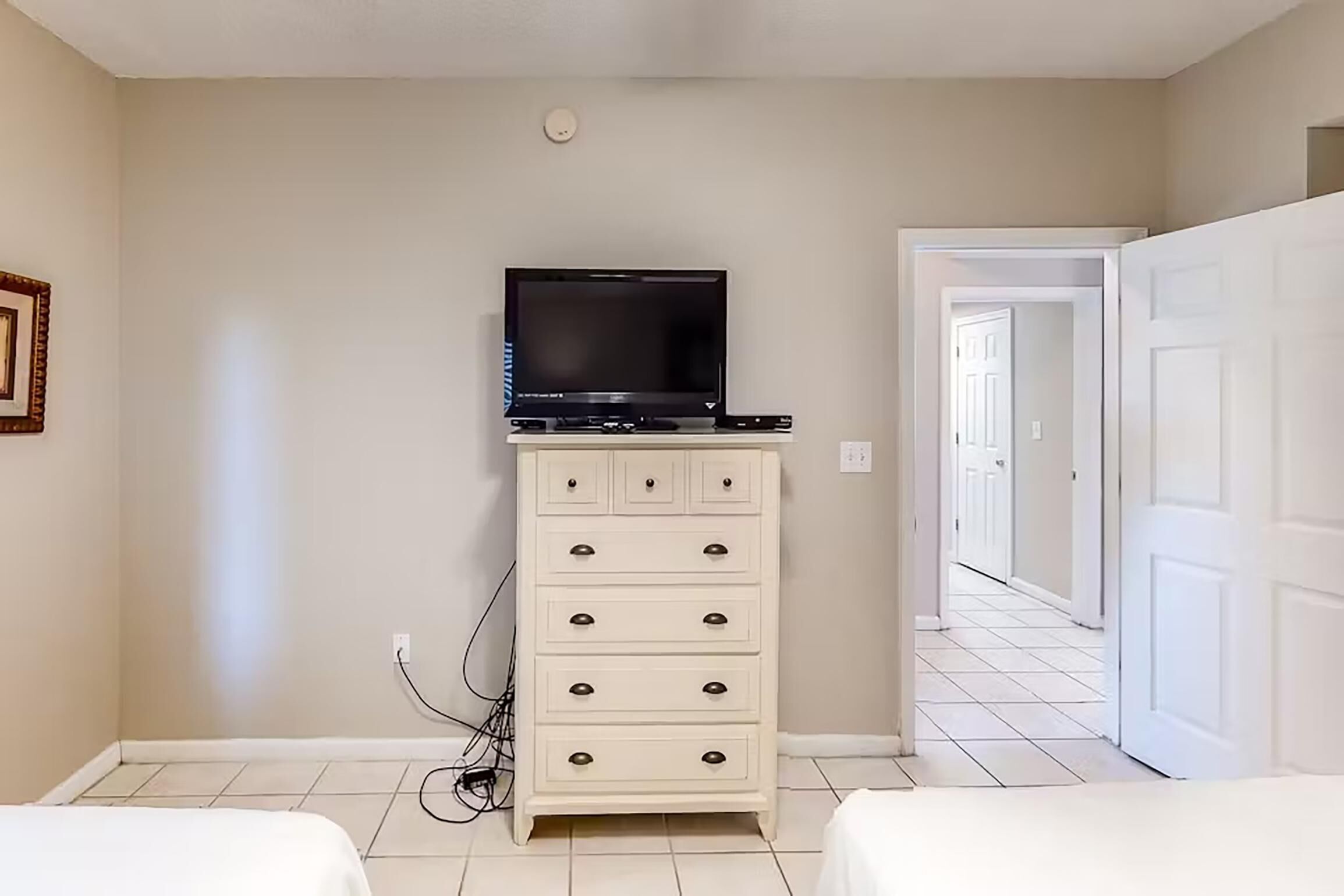 A bedroom with a white dresser, a television on top, and a hallway leading to another room.
