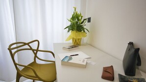 Une pièce avec une chaise jaune, un bureau blanc, une plante en pot, un livre, un stylo, un portefeuille et un sac à main.