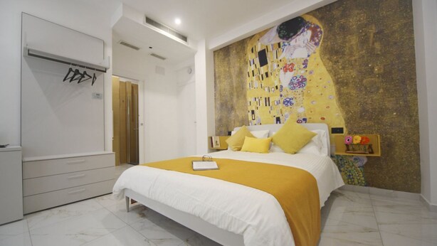 Une chambre à coucher avec un grand lit, une armoire blanche, un tableau au mur et une petite étagère ornée d’objets décoratifs.