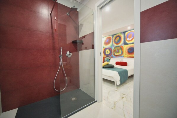 Une salle de bain moderne avec une douche à l’italienne en verre, un lavabo blanc et un tableau abstrait aux couleurs vives accroché au mur.