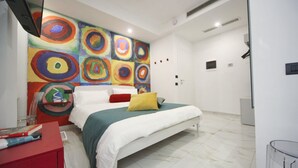 A modern bedroom with a large bed, a colorful abstract painting on the wall, and a red desk with books. - Becoloured Circles Suite. Where it is possible to dream among the masterpieces of art. (Napoli)
