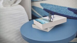 A book with a blue cover on a round blue table in a room with a white bed and a blue and white patterned wall. - Becoloured Wave Suite. Where it is possible to dream among the masterpieces of art. (Napoli)
