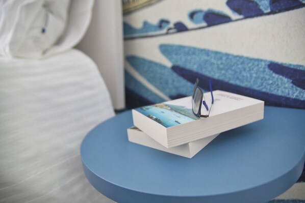 A book with a blue cover on a round blue table in a room with a white bed and a blue and white patterned wall.