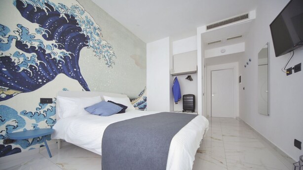A bedroom with a bed, a wall mural, a TV, and a door leading to another room. - Becoloured Wave Suite. Where it is possible to dream among the masterpieces of art. (Napoli)