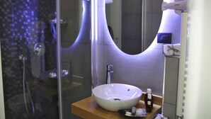Une salle de bain moderne dotée d’un grand lavabo ovale, d’une douche en verre et d’un miroir au design incurvé original.
