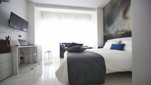 Une chambre moderne avec un lit, un bureau avec un ordinateur portable, une chaise et un grand tableau abstrait accroché au mur.