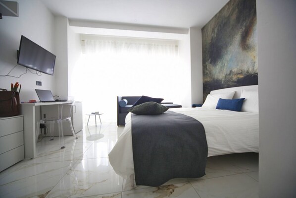 Une chambre moderne avec un lit, un bureau avec un ordinateur portable, une chaise et un grand tableau abstrait accroché au mur.
