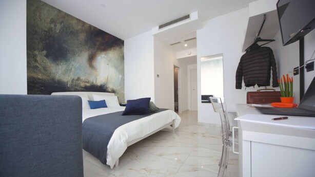 Une chambre moderne avec un grand lit, un bureau avec un ordinateur portable, une chaise et un grand tableau abstrait accroché au mur.