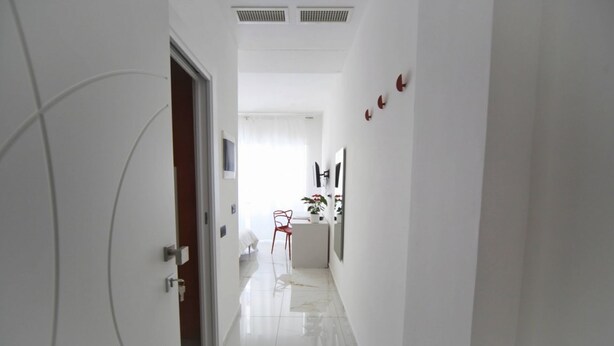A hallway with a white door, a red chair, and a white sofa in the background. - Venice Suite. Becoloured, where it is possible to dream among art masterpieces. (Napoli)