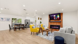 A modern living room with a dining area, a fireplace, and a mounted TV displaying streaming services. - Luxury Newly Renovated Home w/Private Pool+Fire Pit+BBQ Near Downtown&Airport (San Antonio)