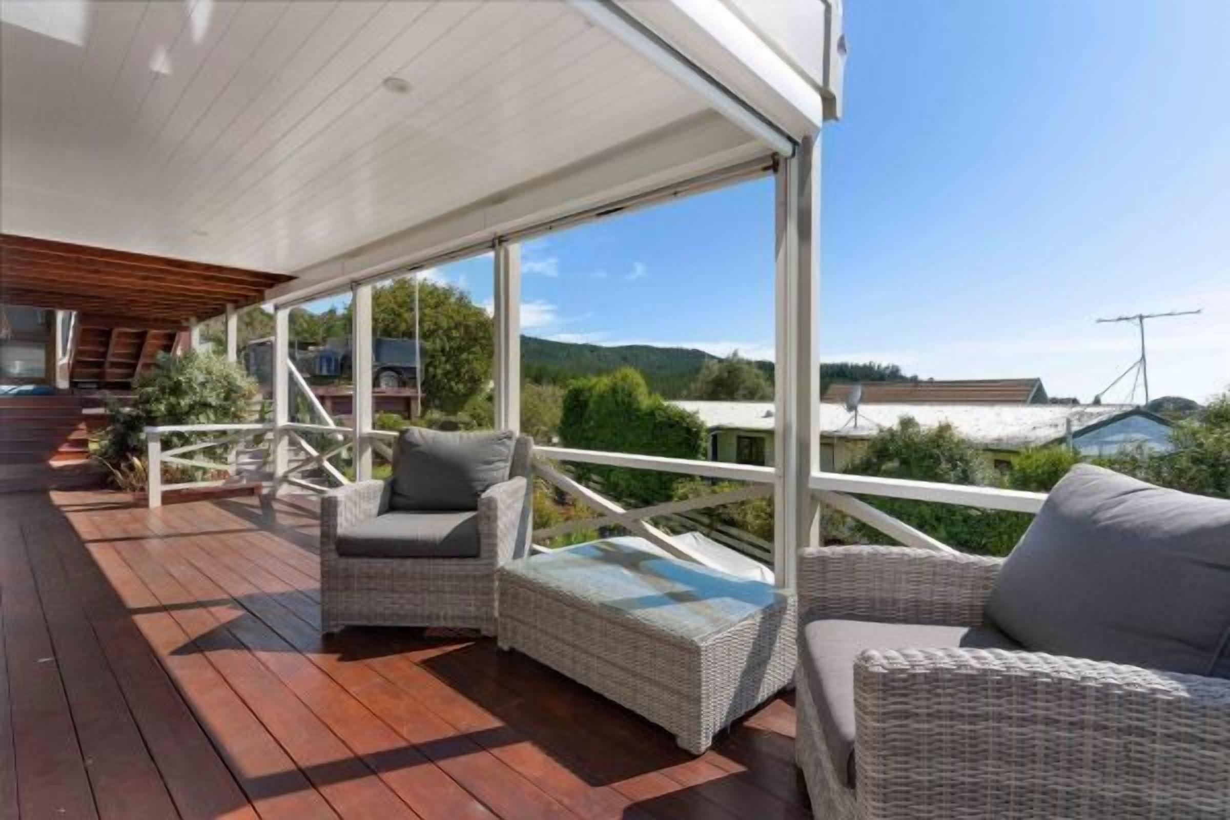 A covered outdoor deck with wicker furniture and a view of the surrounding landscape.