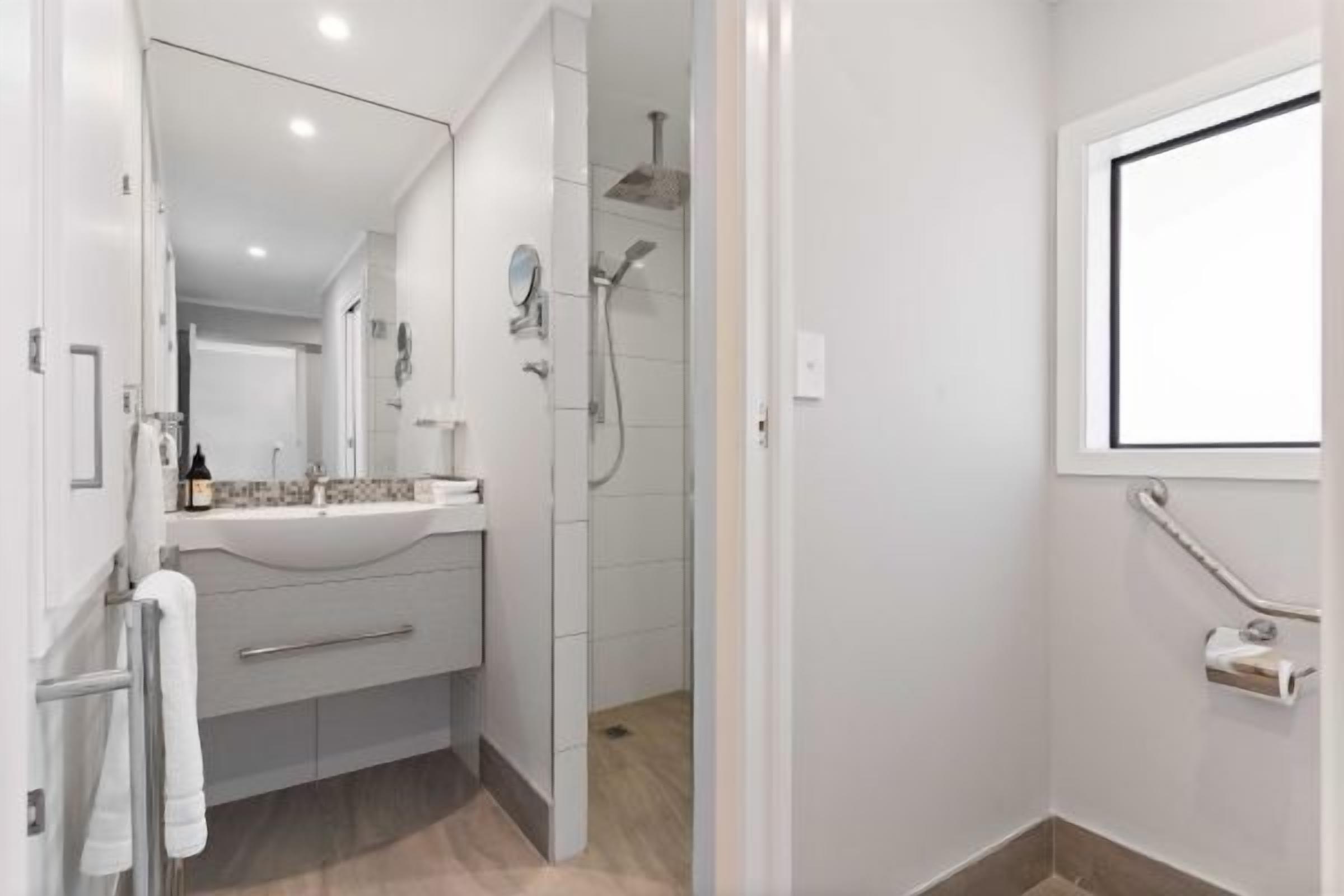 Une salle de bain moderne équipée d’une douche, d’un meuble-lavabo avec miroir et d’un porte-serviettes.
