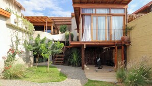 A modern villa with a wooden deck, a covered outdoor seating area, and a small garden with a gravel path. - Casa Kahu by Wynwood House (Los Organos)