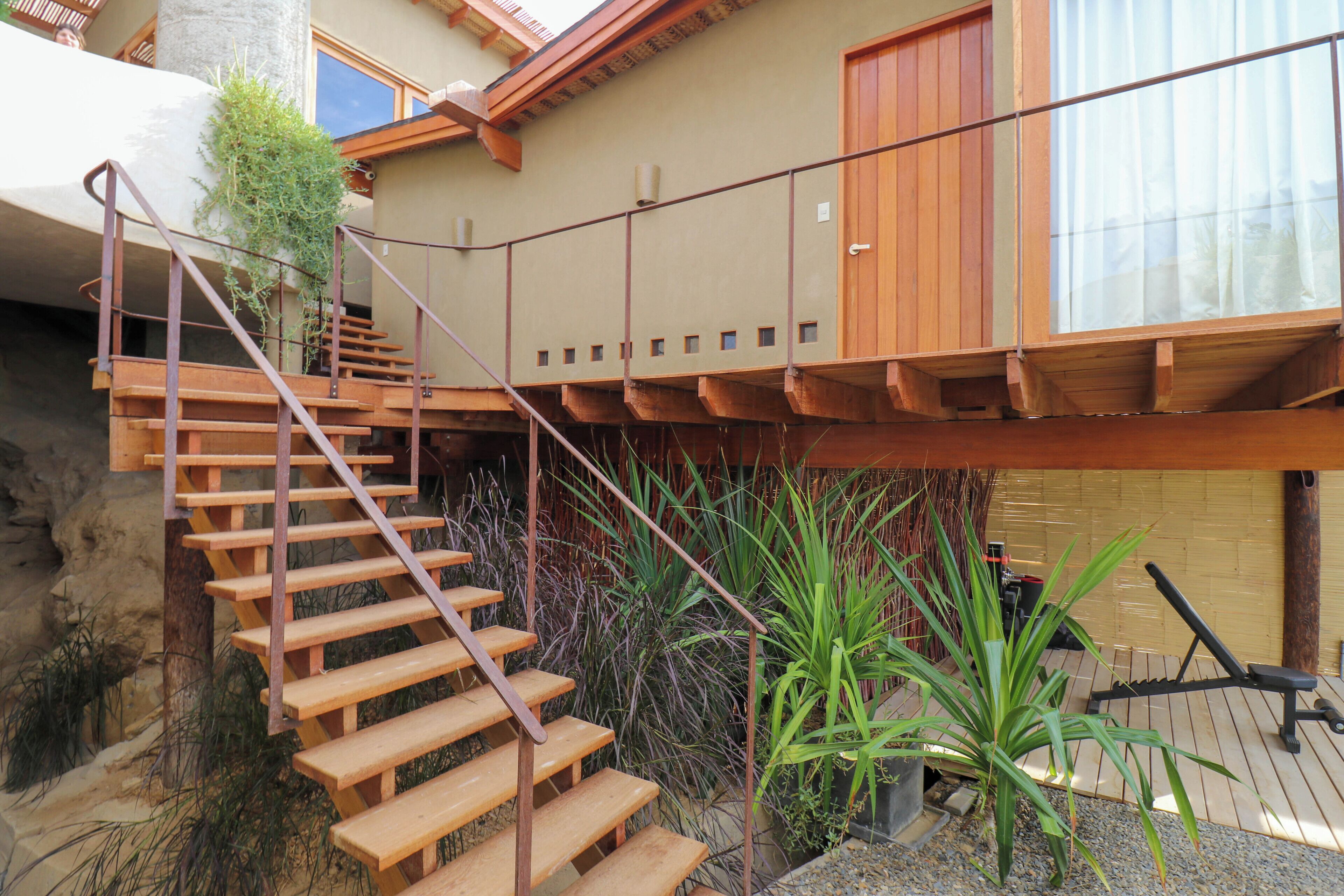 A wooden staircase leading to a balcony with a view of a garden and a wooden deck.