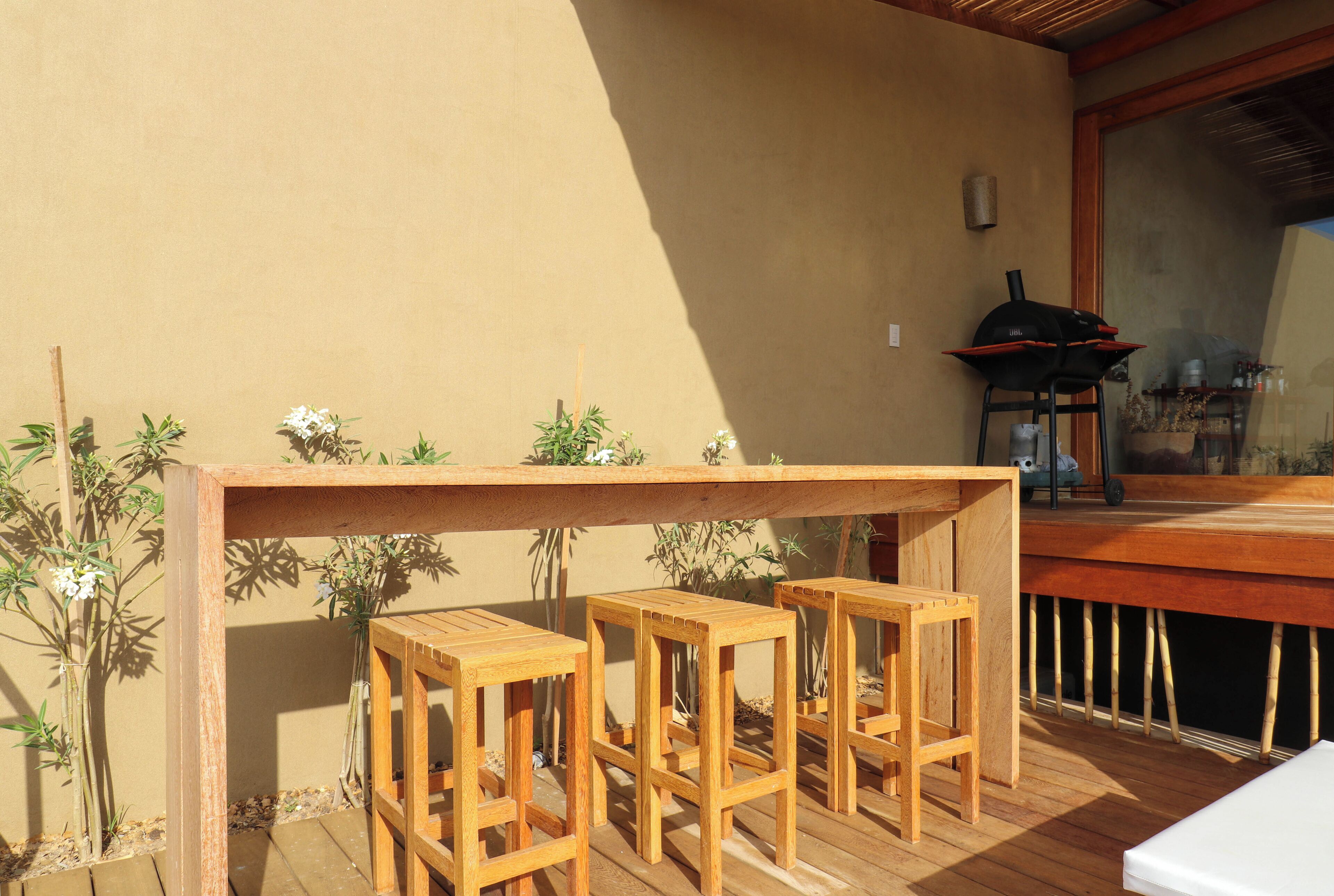 Una terraza de madera con una zona de bar que incluye tres taburetes y una parrilla.