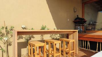 Una terraza de madera con una zona de bar que incluye tres taburetes y una parrilla.