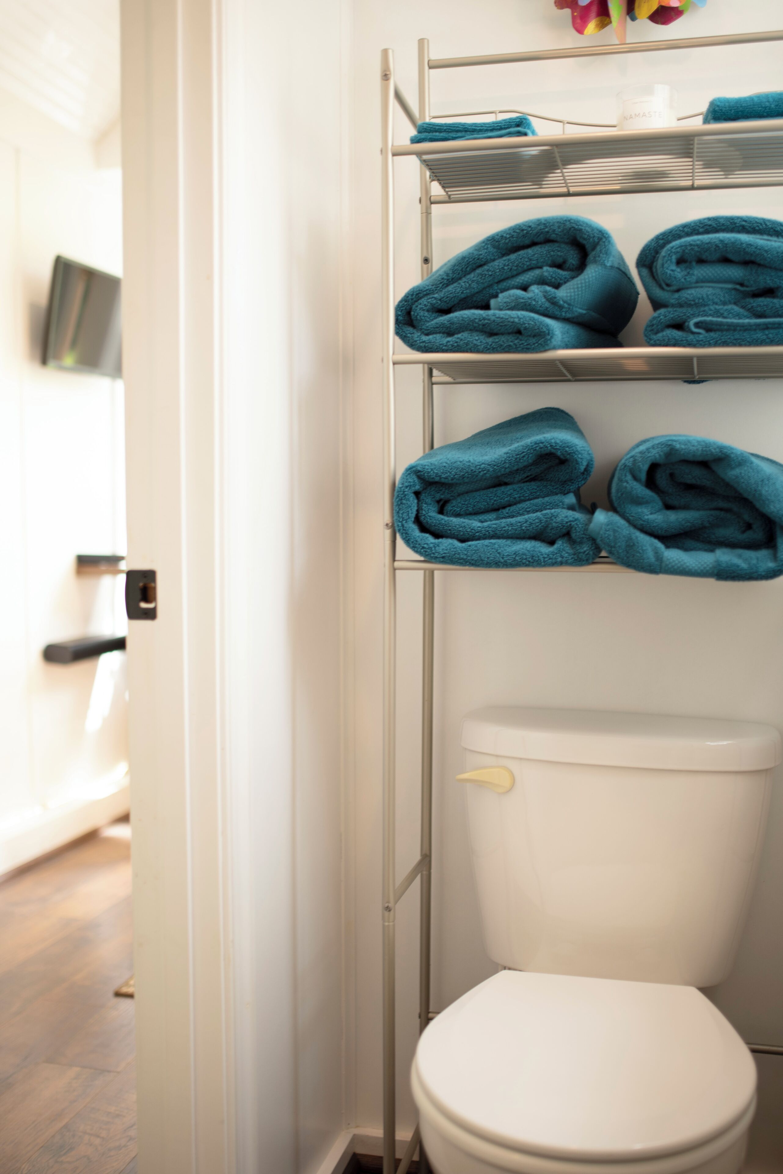 A bathroom with a white toilet, a metal shelf holding folded towels, and a white door.