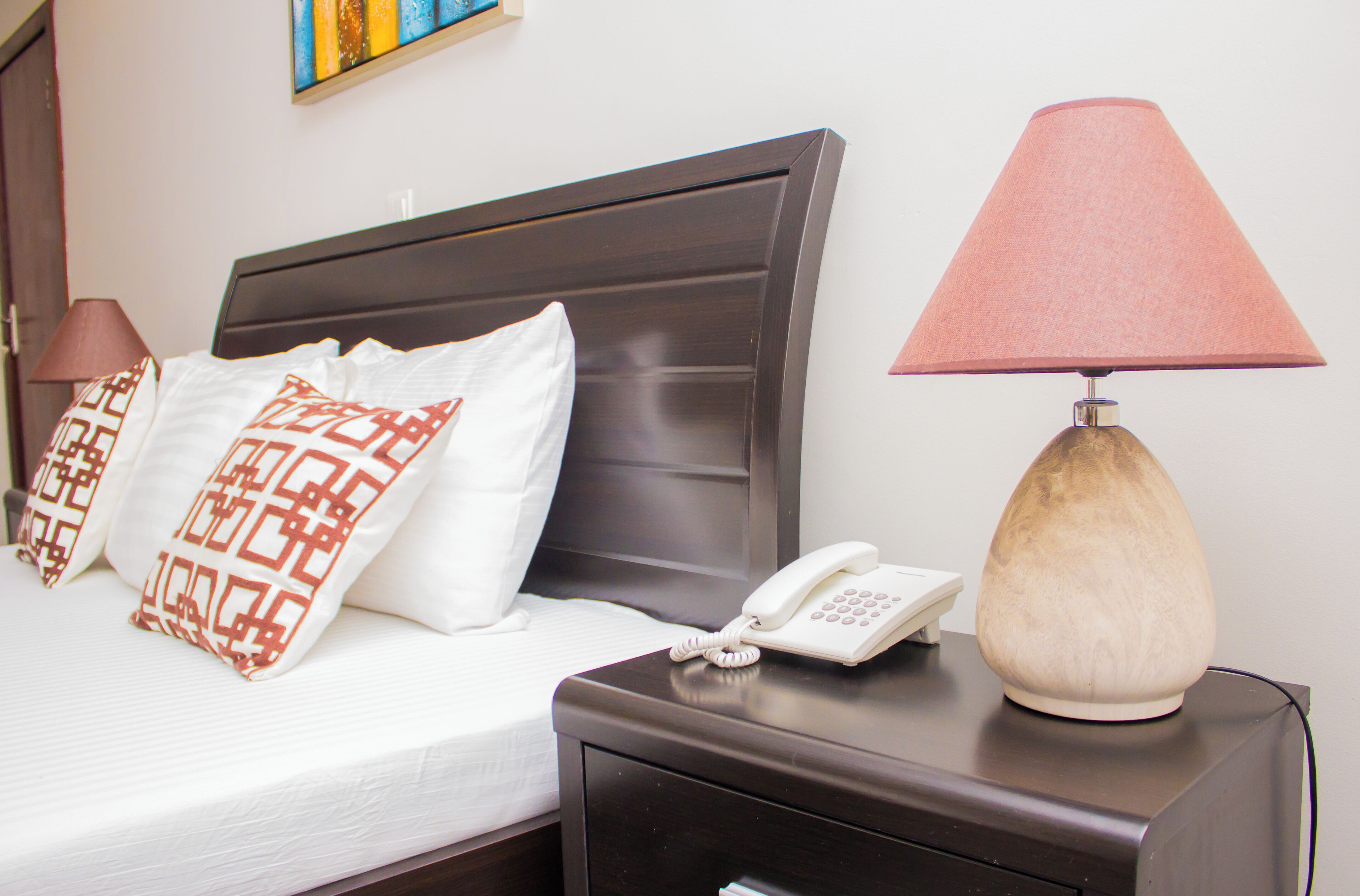 A neatly made bed with patterned pillows, a bedside lamp, and a phone on a nightstand.