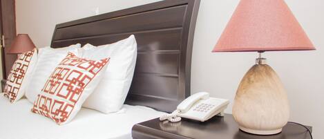 A neatly made bed with patterned pillows, a bedside lamp, and a phone on a nightstand.