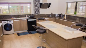 Een moderne keuken met een ingebouwde wasmachine, een groot eiland met barkrukken en een raam met uitzicht op buiten.
