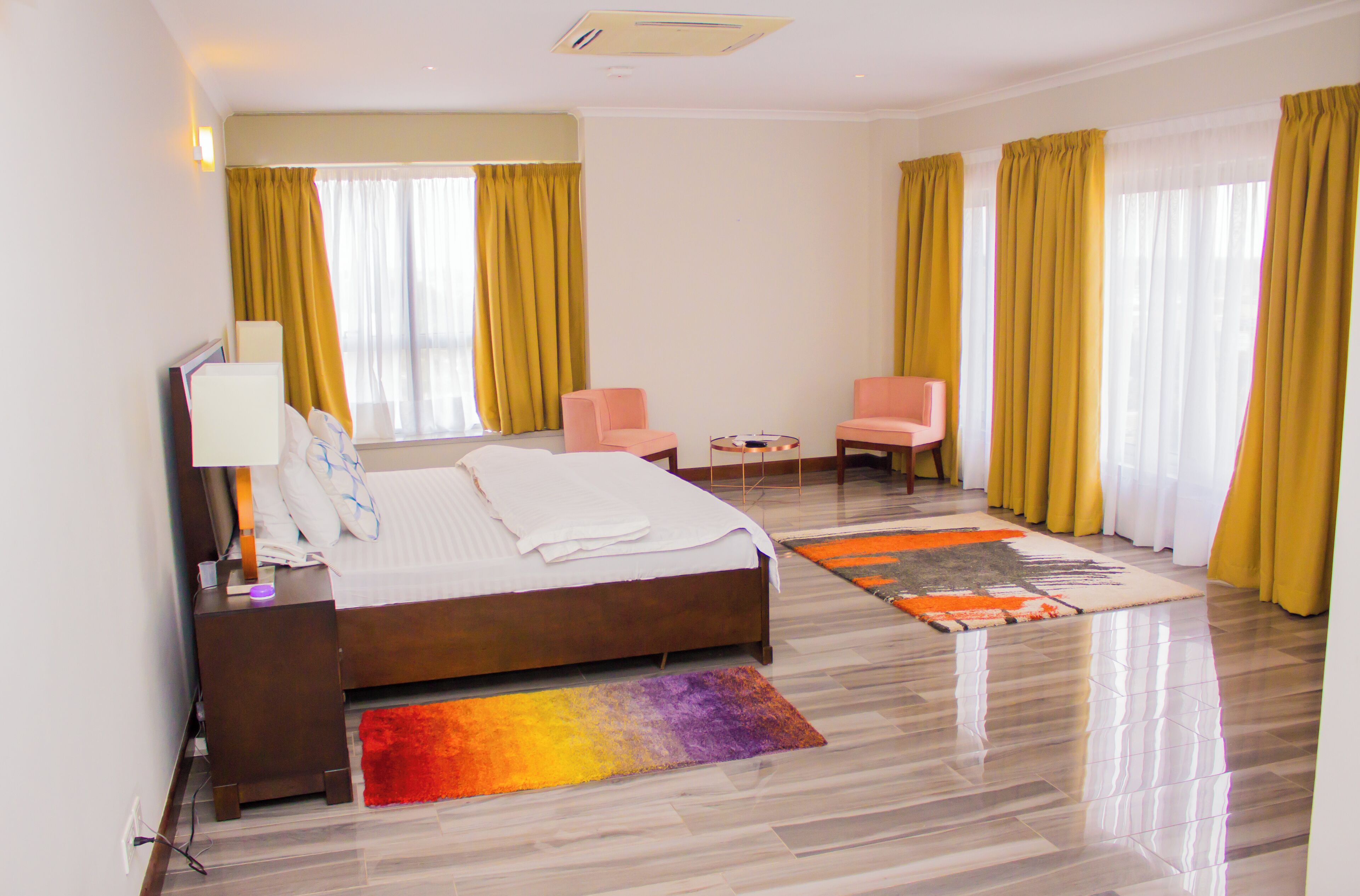 A hotel room with a bed, two chairs, a small table, and a window with curtains.