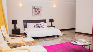 Een hotelkamer met een bed, twee nachtkastjes met lampen, een klein rond tafeltje met een tijdschrift, twee gele stoelen en een roze vloerkleed.