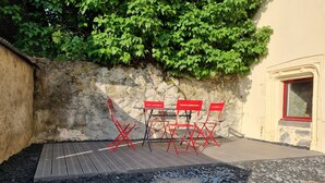 A patio area with a wooden deck, red folding chairs, and a stone wall with greenery.