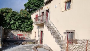 A building with a stone staircase leading to a balcony, a small door, and a window with a curtain.