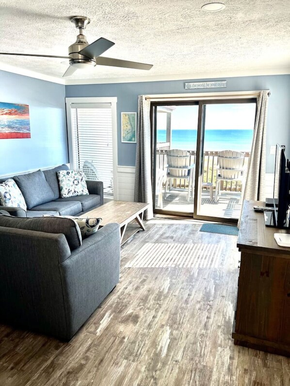 A living room with a gray couch, wooden coffee table, and a view of the ocean through a sliding glass door.