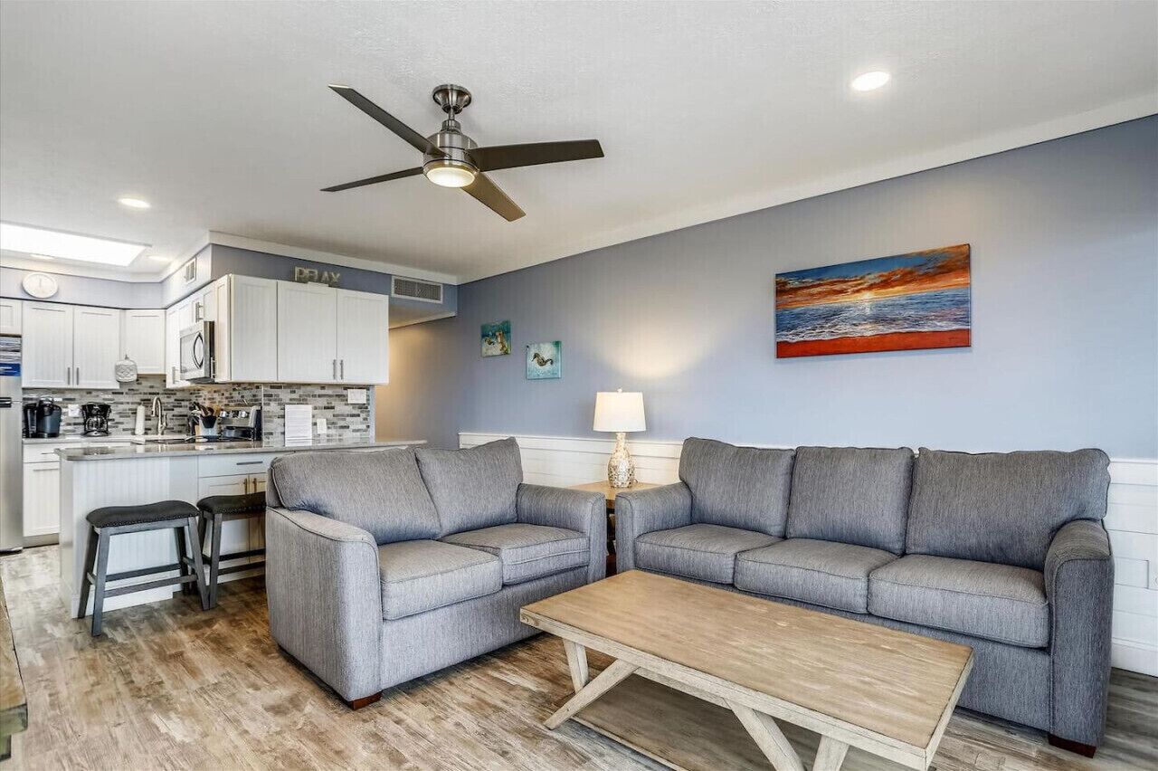 Ein modernes Wohnzimmer mit zwei grauen Sofas, einem Holztisch und einem Deckenventilator.