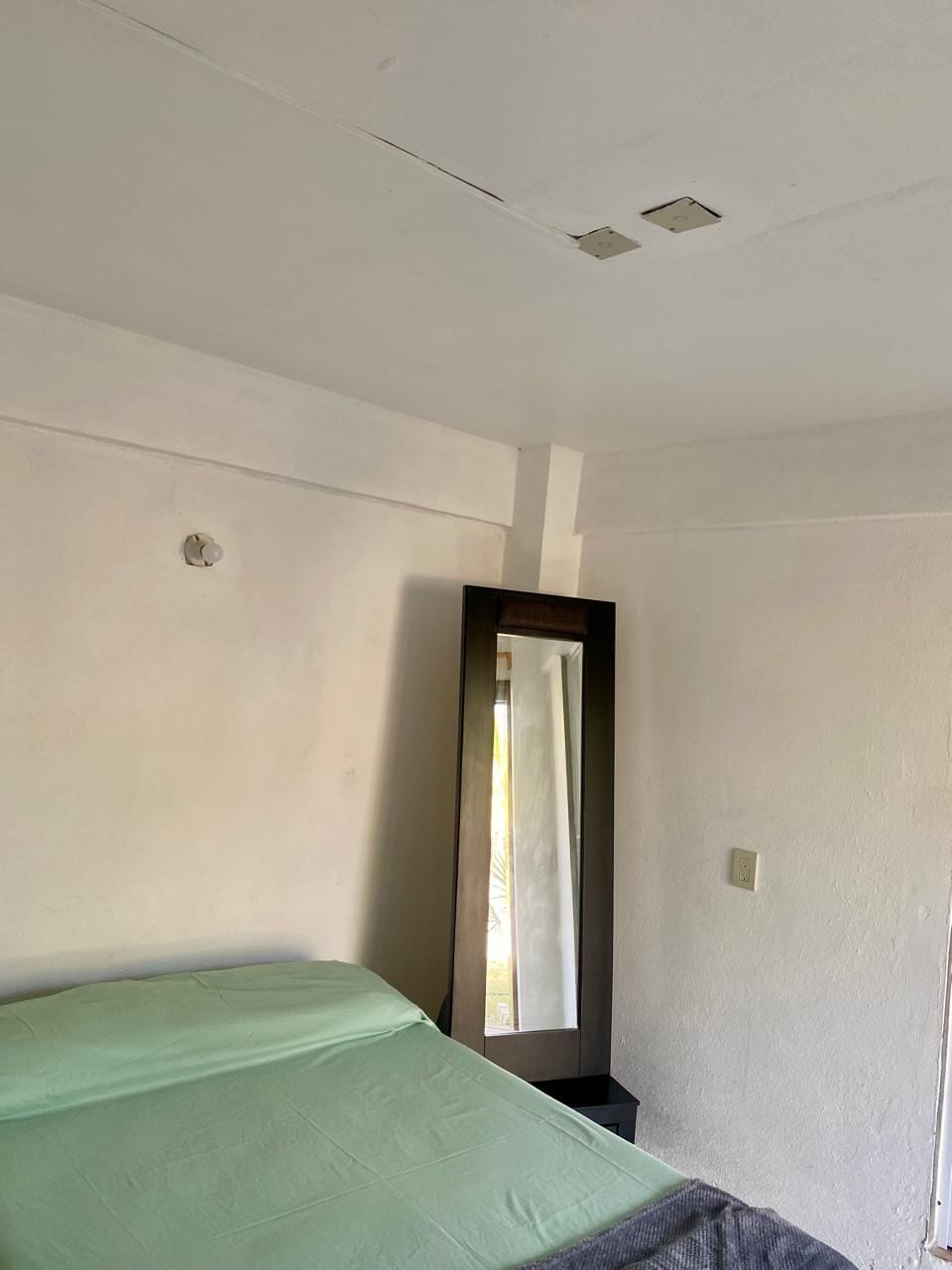 Una stanza essenziale con un letto, uno specchio e una finestra.