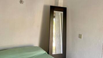 Una stanza essenziale con un letto, uno specchio e una finestra.
