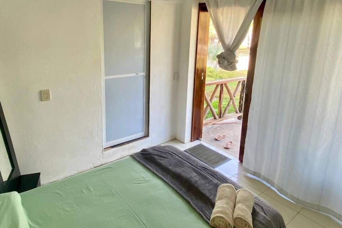 A room with a bed, a door, and a view of the outside.