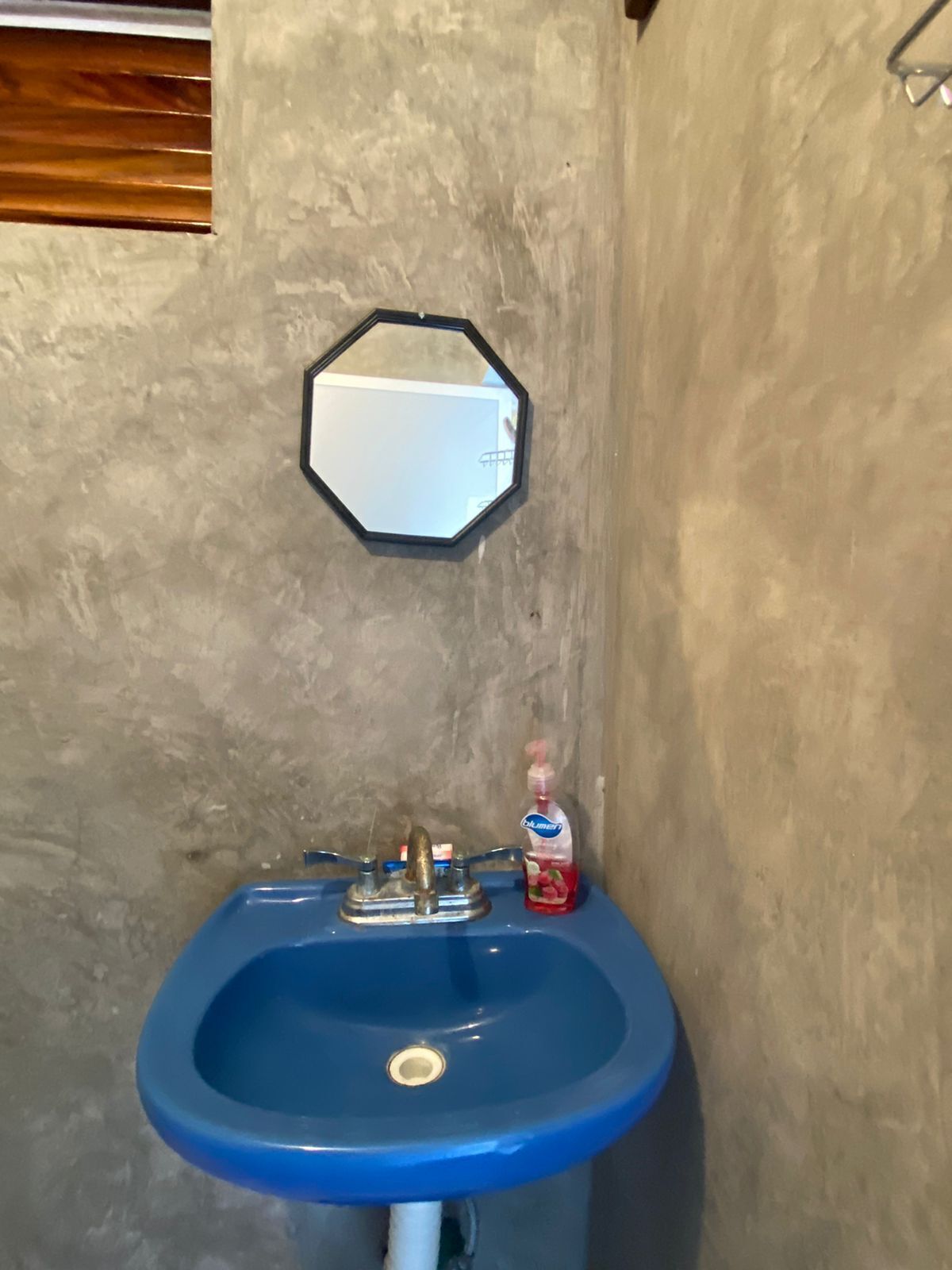 Een badkamer met een blauwe wasbak, een spiegel en een fles vloeibare zeep.