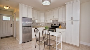 A modern kitchen with white cabinets, a stainless steel refrigerator, and a dining table with two chairs.