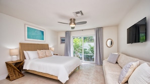 A bedroom with a bed, a nightstand, a ceiling fan, a TV, and a view of the outdoors.