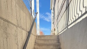 Un escalier en béton avec des rampes en métal, menant à un bâtiment à la façade blanche.