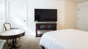 Une chambre d’hôtel avec un lit, un téléviseur posé sur une commode en bois, une chaise et une petite table.