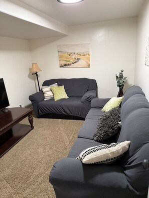 A living room with a dark grey sectional sofa, a wooden coffee table, a floor lamp, and a painting on the wall.