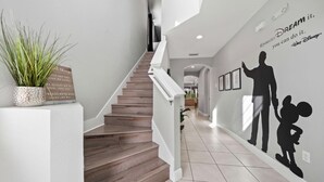 A staircase with a white railing, a potted plant, and a wall with silhouettes and a motivational quote. - Ohana Dream 6 bedrooms, 5 bathroom, private pool, 10 mins from Disney!  (Kissimmee)
